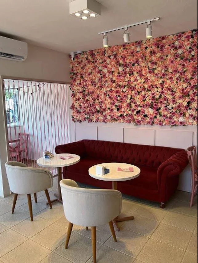 Salão da Bolinhas de Amor, com parede de flores rosa, sofá vinho e mesas redondas